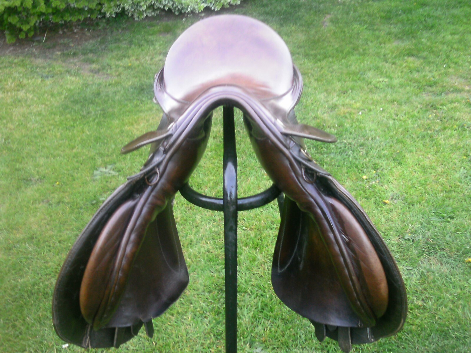 Silla de montar de cuero marrón sobre soporte metálico negro, colocada en césped verde con tonos terrosos suaves